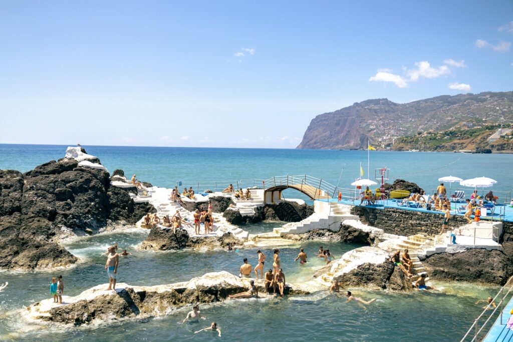 Badende in den Meeresbecken Doca do Cavacas zwischen Lavafelsen in Funchal auf Madeira, dahinter die Steilküste