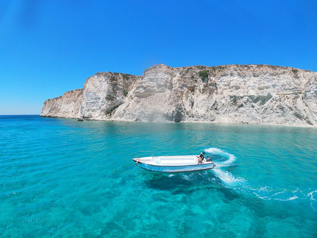 Motorboot im türkisen Wasser vor einer weißen Felsküste auf Kreta