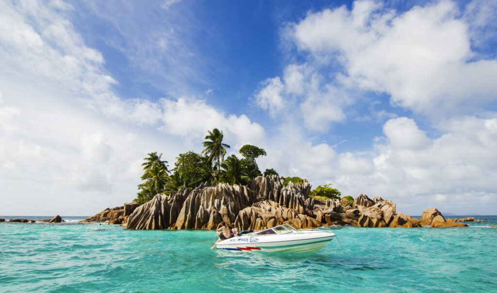 Kleine Granitinsel mit Palmen vor den Seychellen, davor ein Motorboot im türkisen Wasser